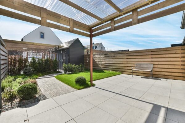 A sunny garden with a paved patio and wooden garden blinds providing shade.