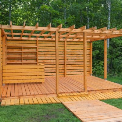 A wooden structure with a pergola and floor made of wooden slats in a forest setting.